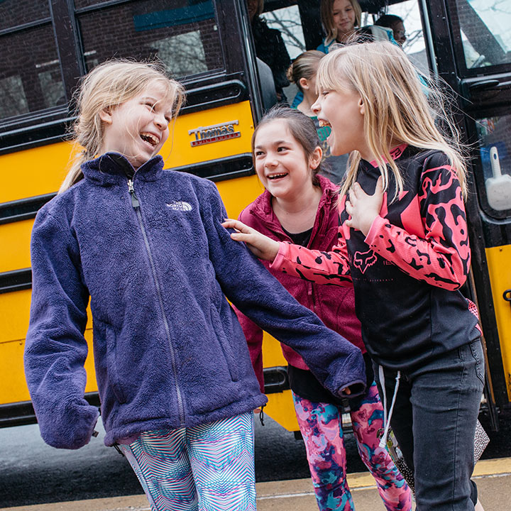 Our Journey Continues A group of 3 girls getting off of a school bus laughing together